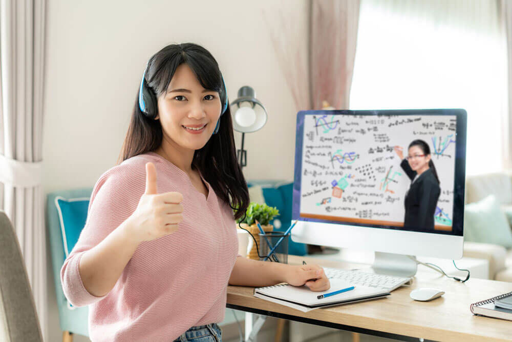 Jeune fille avec un casque d’écoute devant un écran d’ordinateur, qui fait face à l’objectif avec un sourire et le pouce levé.